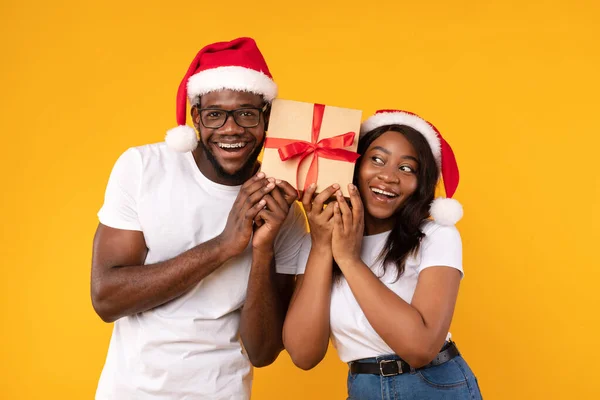 Μαύρο ζευγάρι κρατώντας χριστουγεννιάτικο δώρο μαντέψουν τι είναι μέσα, κίτρινο φόντο — Φωτογραφία Αρχείου