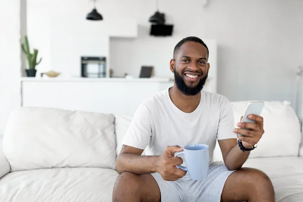 Hombre negro mensajes de texto en su teléfono inteligente beber café —  Fotos de Stock