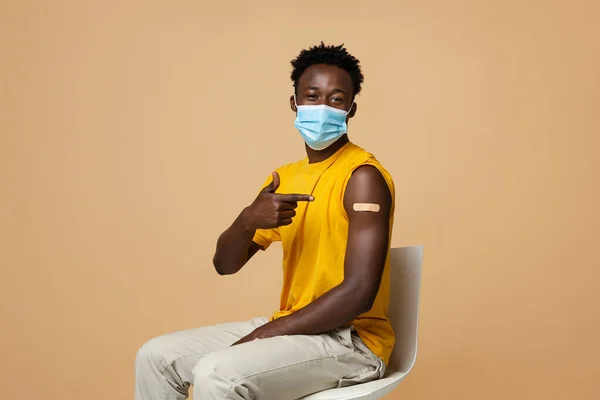 Vaccinationskampanj. Svart kille i medicinsk mask pekar på armen med gips — Stockfoto