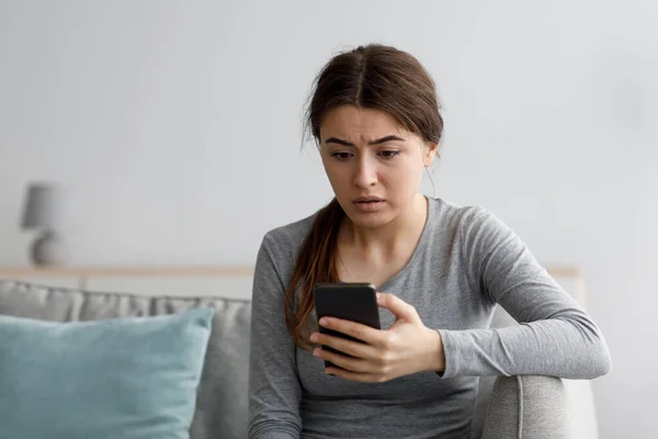 Inquiet triste choqué dépressif attrayant jeune femme européenne regardant téléphone à l'intérieur de la maison — Photo