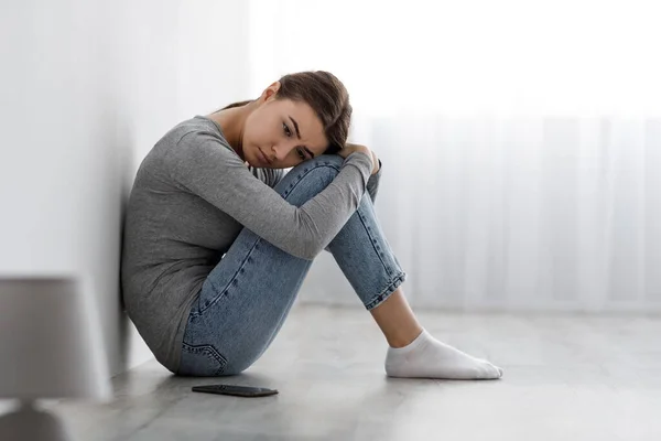 Uttråkad upprörd deprimerad dam sitter på golvet med smartphone, ser likgiltig till sidan har problem — Stockfoto
