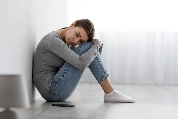 Gelangweilte aufgebrachte depressive Dame sitzt mit Smartphone auf dem Boden und schaut gleichgültig auf die Seite, die Probleme hat — Stockfoto