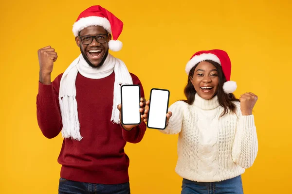 African American Couple Showing Phones Screens Wearing Santa Hats, Studio — Stock Photo, Image