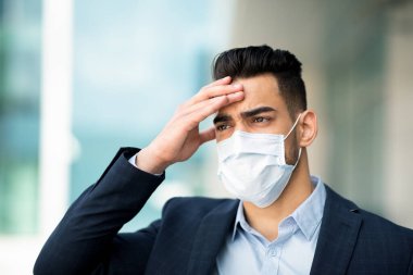 Stresli orta doğulu iş adamı maske takıyor. Kafaya dokunuyor, iş başarısızlığı yaşıyor.