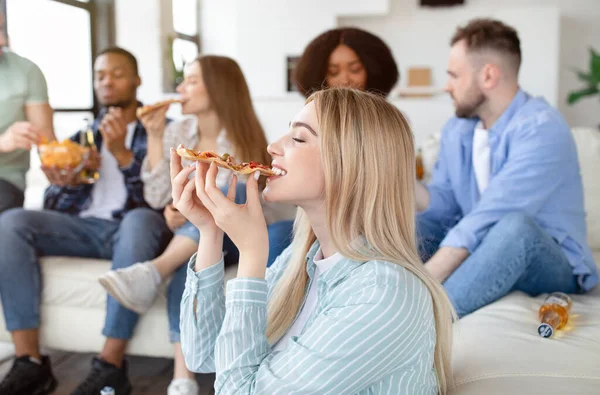 Mooie jonge blonde dame eten pizza op home party met haar multi-etnische vrienden, vrije ruimte — Stockfoto