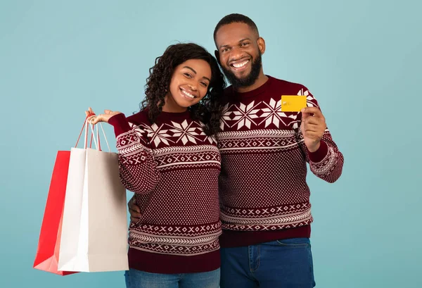 Noel hediyeleri. Mutlu siyah kadın ve erkek arkadaşı alışveriş torbaları ve kredi kartı, mavi arka plan — Stok fotoğraf
