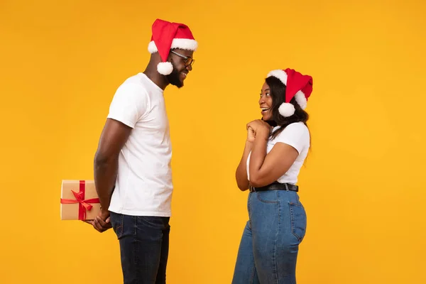 Hombre africano sosteniendo el regalo de Navidad detrás de la espalda Mujer felicitante, Estudio — Foto de Stock