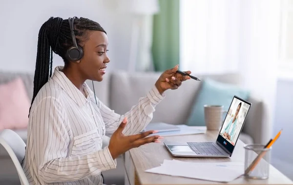 Jonge Afro-Amerikaanse dame in koptelefoon oproepen online en kijkt video les met leraar op het scherm, studies thuis — Stockfoto