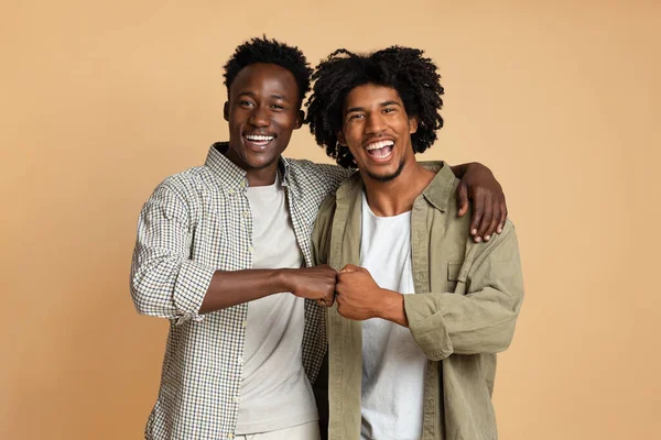 Retrato de dos alegres chicos negros abrazando y haciendo el gesto de golpe de puño —  Fotos de Stock