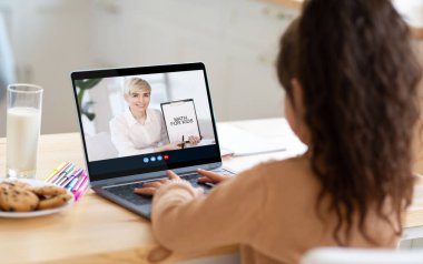 Küçük kız öğrenci, yetişkin beyaz kadın öğretmenle video görüşmesi yapıyor. Evde dizüstü bilgisayarda matematik dersi veriyor.