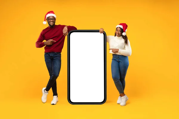 Black Couple Pointing At Phone Screen Het dragen van Santa hoeden, Studio — Stockfoto