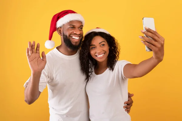 Glad afrikansk amerikansk par video samtal till familjen under nyår och jul semester, gul bakgrund — Stockfoto