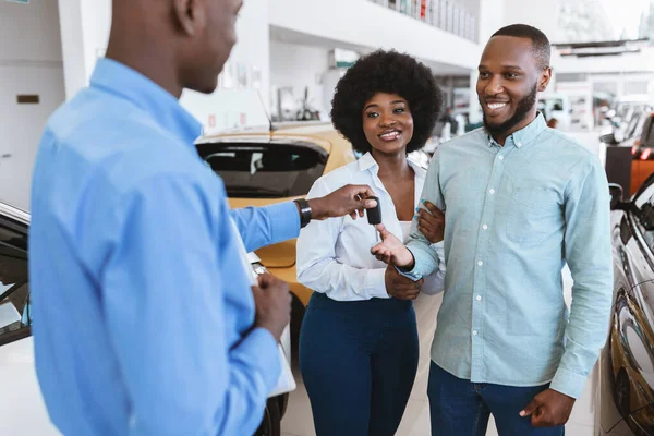 Vendedor dando chave de carro para jovem casal negro na concessionária de automóveis. Conceito de distribuição local do veículo — Fotografia de Stock