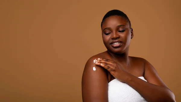 Mooie jonge zwarte vrouw aanbrengen lichaam moisturizer op schouders — Stockfoto