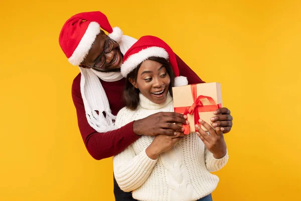 アフリカ系アメリカ人の夫クリスマスの贈り物、黄色の背景を与える驚くべき妻 — ストック写真