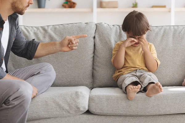 Kindermishandeling concept. Ongelukkig jongetje zit op de bank en huilt, onherkenbare boze vader schreeuwt tegen overstuur kind — Stockfoto