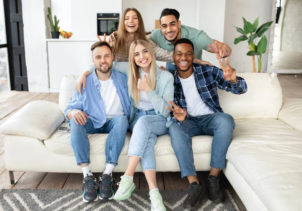Grupo internacional emocional de amigos sentados no sofá em casa, mostrando gestos diferentes, sorrindo para a câmera — Fotografia de Stock