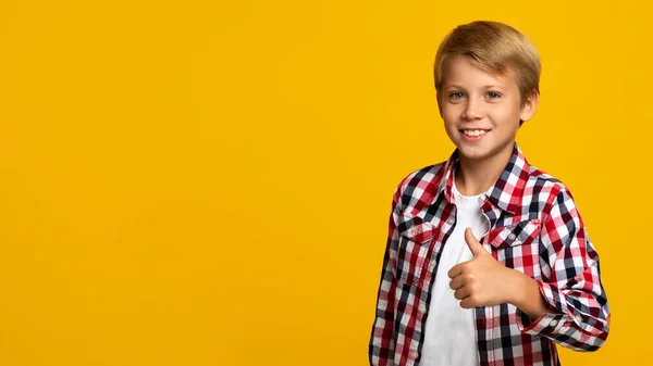 Alegre confiado europeo adolescente chico mostrando pulgar arriba mirando cámara, en amarillo fondo — Foto de Stock