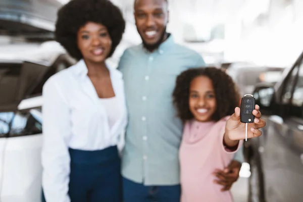 Adorável menina afro-americana mostrando chave do carro, posando com seus pais na concessionária de automóveis, foco seletivo — Fotografia de Stock