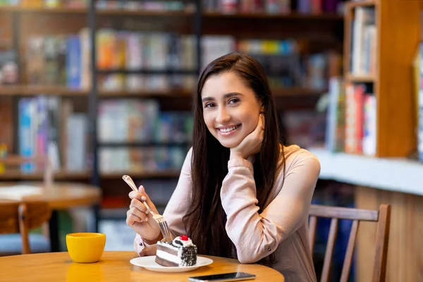 예쁜아 라브 여성 이 카페에 앉아서 카메라 앞에서 웃으면서 디저트와 커피를 즐기고 있습니다. — 스톡 사진