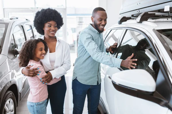 Família preta feliz selecionando carro novo no showroom automático. Conceito de distribuição local do veículo — Fotografia de Stock