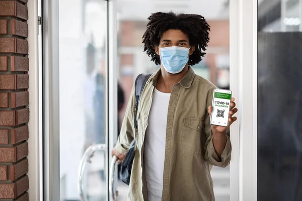 Young African Man Demonstrating International Covid-19 Certificate On Smartphone On Building Entrance — Stock Photo, Image