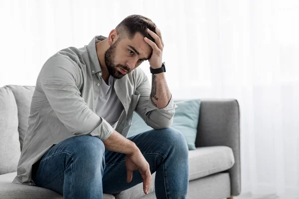Uomo seduto da solo sentendosi triste preoccupazione rimpianto o paura, depresso e disperato nel divano di casa — Foto Stock