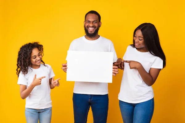 Zwarte familie met blanco wit reclamebord in de gele studio — Stockfoto