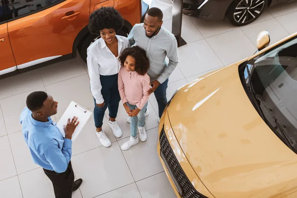 Visão superior da jovem família negra comprando ou alugando carro novo, falando com vendedor na concessionária de automóveis — Fotografia de Stock