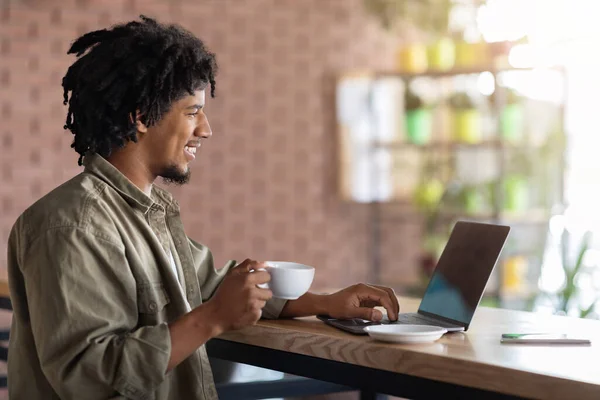 Giovane ragazzo freelancer nero che lavora con il computer portatile e bere caffè al caffè — Foto Stock