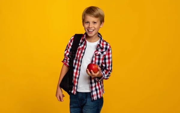 Wesoły pozytywny europejski nastolatek chłopiec uczeń z plecakiem trzyma czerwone jabłko i gotowy do nauki — Zdjęcie stockowe