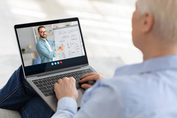 Viejo europeo hombre estudia de forma remota, ve lección en línea y aprende Inglés con el joven tutor en la pantalla del ordenador portátil — Foto de Stock