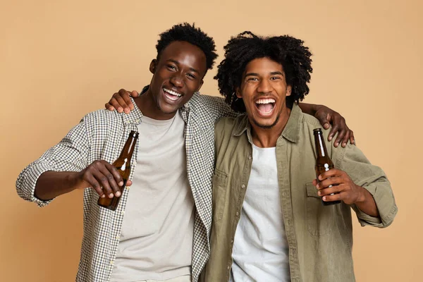 Retrato de dos felices amigos negros abrazando y sosteniendo botellas con cerveza —  Fotos de Stock