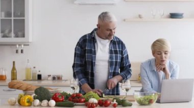 Evde mutfaktaki dizüstü bilgisayarla Olgun Çiftler Yemek Yemeği