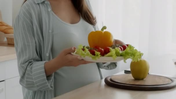 Mujer embarazada sosteniendo placa con verduras frescas, tomando y comiendo tomate de cereza — Vídeo de stock