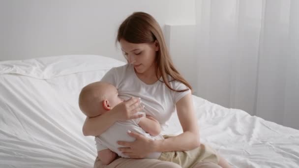 Young mother breastfeeding her infant baby while sitting on bed at home — Stock Video