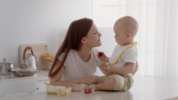 Schattige baby voeden moeder met aardbei tijdens het hebben van snacks in de keuken — Stockvideo