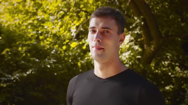 Conceito de estilo de vida saudável. Jovem desportivo virando cara para câmera e sorrindo, posando no parque público na manhã ensolarada — Vídeo de Stock