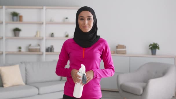 Junge positive Frau aus dem Mittleren Osten trägt Hijab, lächelt in die Kamera und trägt nach dem Sport eine Wasserflasche — Stockvideo