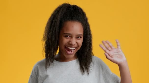 Funny afroamericana adolescente agitando la mano sobre fondo amarillo — Vídeos de Stock