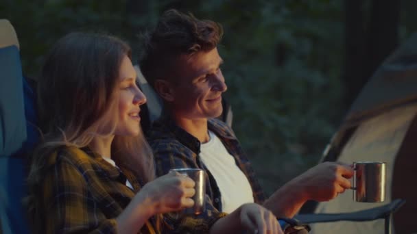 Junger Mann und Frau trinken Tee am Lagerfeuer, zelten abends im Wald, Nahaufnahme Porträt, Zeitlupe — Stockvideo