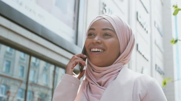 Portrait extérieur d'une jeune femme musulmane afro-américaine heureuse portant un foulard traditionnel parlant sur son téléphone portable — Video