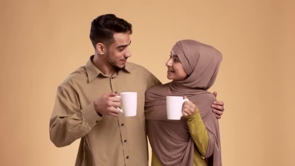 Feliz pareja musulmana bebiendo café y hablando abrazos, fondo beige — Vídeo de stock