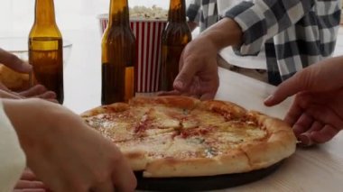 Bir grup arkadaş ev partisinde tahta tabaktan pizza dilimleri alıyor.