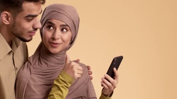 Spændt muslimsk par ved hjælp af smartphone stående over Beige Studio baggrund – Stock-video