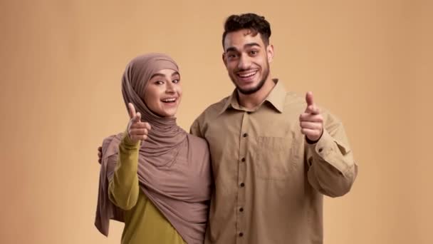 Modernes Paar aus dem Nahen Osten zeigt mit dem Finger auf Kamera auf beigem Hintergrund — Stockvideo