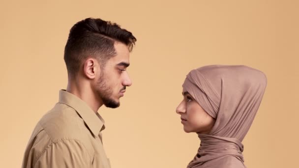 Серьёзная мусульманская пара поворачивается лицом к камере, бежевый фон — стоковое видео