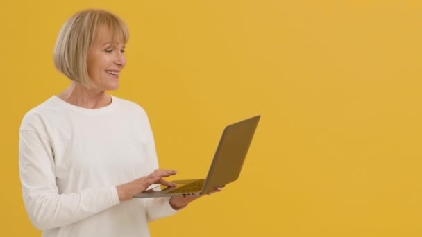 아름다운 나이드신 분 이 노란 녹음실 뒤에서 있는 동안 노트북 컴퓨터를 사용하는 모습 — 비디오