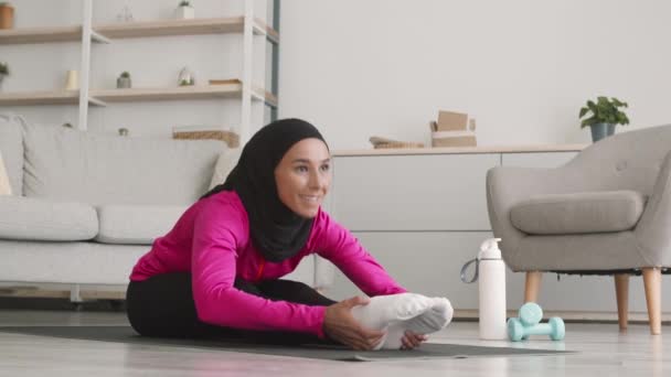 Formación en flexibilidad. Joven mujer flexible de Oriente Medio con traje deportivo y hijab estirando su cuerpo en casa — Vídeos de Stock