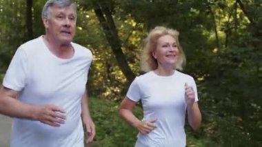 Sportif yaşlanma kavramı. Halka açık parkta kardiyo antrenmanı yapan yaşlı bir adam ve kadın. Atışı takip edin.